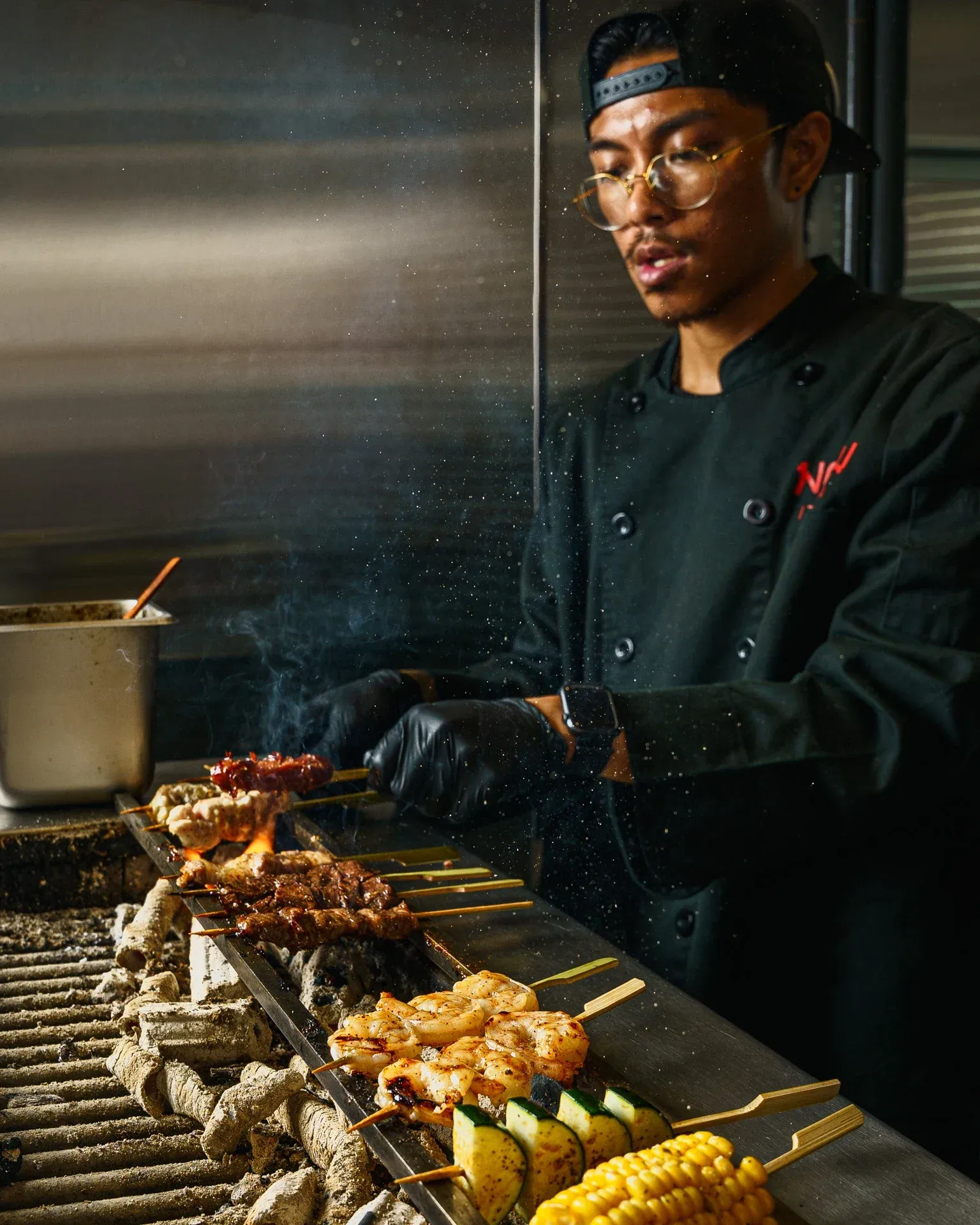 Chef grilling yakitori skewers with corn, shrimp, and meat over charcoal
